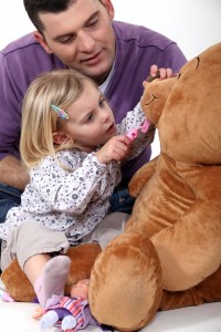 Father and daughter playing dentist with a teddy bear